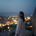 A female tourist is enjoying looking over the city from the rooftop of the hotel at night where she is staying during her travel.