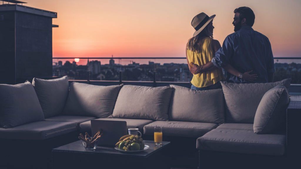 Back view of happy couple in love relaxing on sofa at penthouse patio and communicating. Copy space.